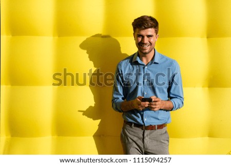 smiling elegant smart guy with cellphone standing on a yellow background