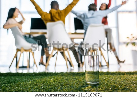 selective focus of glass of water and multiethnic business people sitting at table in office