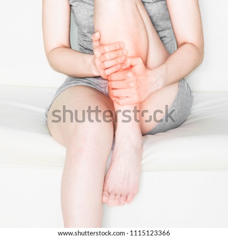woman wearing gray clothes with leg pain .Acute pain in a woman ankle. Female holding hand to spot of ankle-ache. Concept photo with read spot indicating location of the pain.Health care concept