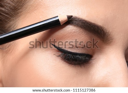 Young woman correcting shape of eyebrow with pencil, closeup