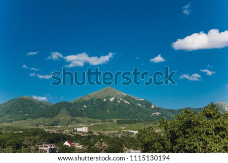 Mountains with clouds and blue sky. Summer. Trees and fields. Small houses. Russia