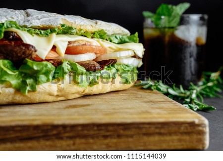 big sandwich  on black background rosemary cucumber wooden board Street food, fast food. Homemade burgers with beef, cheese  on the wooden table. Glass of cola with ice, mint