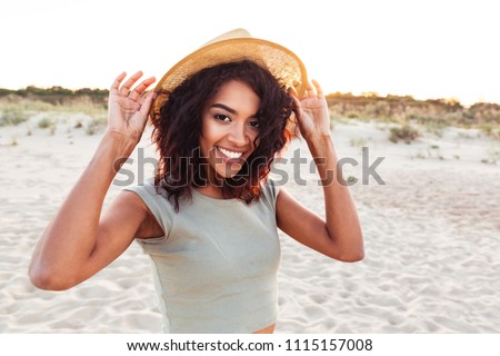 Close up of smiling young african girl in summer hat looking at camera at the beach
