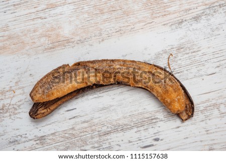A spoiled banana on a wooden background. White worms on a berry. Small pests. Larvae of flies in a banana