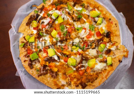 Pizza made of toasted corn taco tortilla with meat, tomato, onion, cream and sauces, Mexican style.