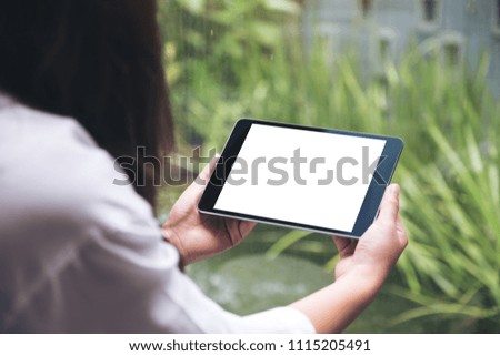 Mockup image of woman's hands holding black tablet pc with blank white desktop screen and green nature background