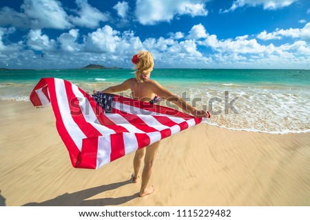 Back side Hawaiian woman holding a waving American flag in American flagged bikini. Tropical Lanikai Beach, east shore of Oahu in Hawaii, USA. Freedom and 4th July patriotic concept.
