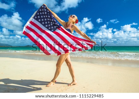 Smiling woman with american flag bikini waving american flag in spectacular tropical Lanikai Beach, east shore of Oahu in Hawaii, USA. Enjoying and freedom and 4th July patriotic concept.