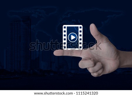 Play button with movie icon on finger over world map and modern city tower, Cinema online concept, Elements of this image furnished by NASA