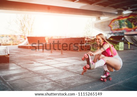 A picture of nice girl sitting in squat position. She is stretching her left leg and trying to keep balance. Girl is holding right hand on the edge of roller.