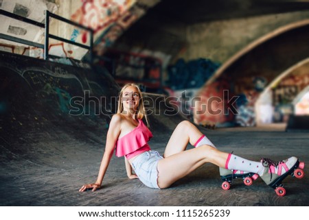 Pretty rollerblader is sitting on the concrete ground and looking to the side. She is smiling. This model is tired after intensive workout. She is posing and having some rest.
