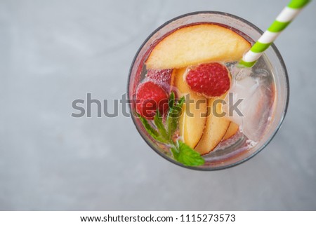Homemade iced lemonade or tea with ripe peaches and Raspberries. Grey background. Top view, space for text