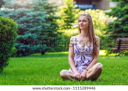 Portrait of pretty, young, cheerful woman sitting on green grass and rests, legs crossed
