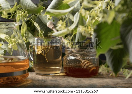 Glass of linden tea with honey and flowers on wooden table.