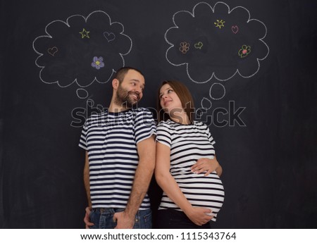 portrait of husband and pregnant wife posing against black chalk drawing board
