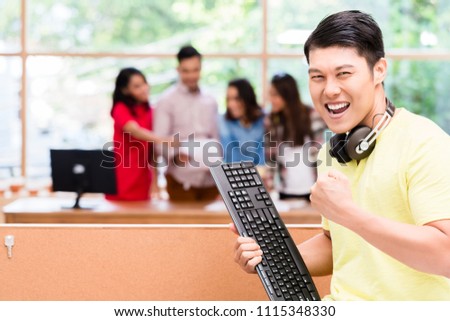 Portrait of young Chinese employee happy for his successful work on computer and for his contribution to the success of the team
