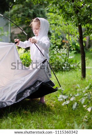 Child girl is setting up tourist tent. Summer travel, camping or hiking concept
