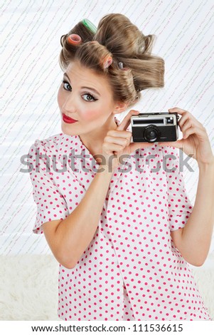 Portrait of beautiful young woman with hair curlers holding an old fashioned digital camera