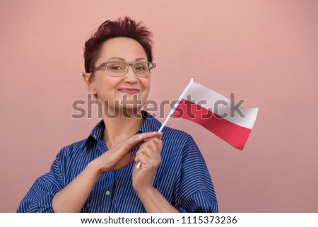 Woman holding flag of Poland. Nice portrait of middle aged lady 40 50 years old with a national Polish flag over pink wall background.Learning Polish language. Visit Poland concept. Royalty-Free Stock Photo #1115373236