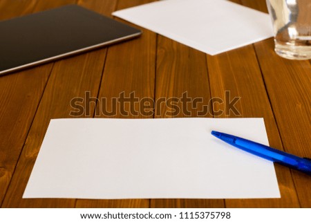 Workplace with a blank paper, blue pencil on a wooden table; tablet and a glass of water in the back