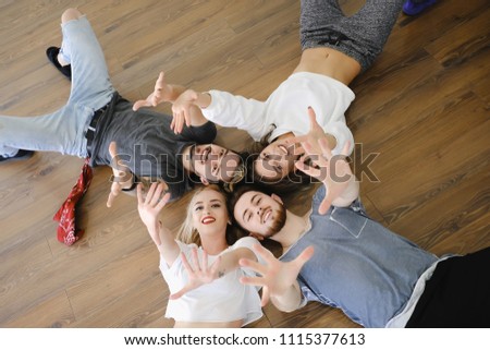 Top view four cheerful young people laying on the floor had by head, showing victory, peace sign, holding hands up, smiling, having fun together.