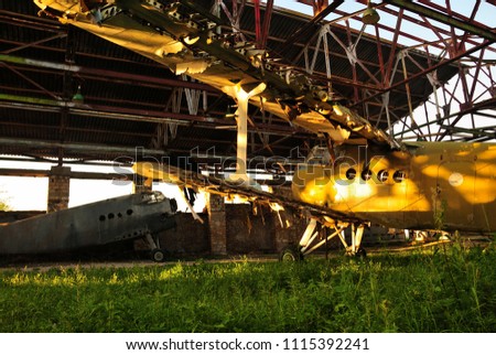 Old retro broken airplane in an abandoned destroyed hangar in the setting sun