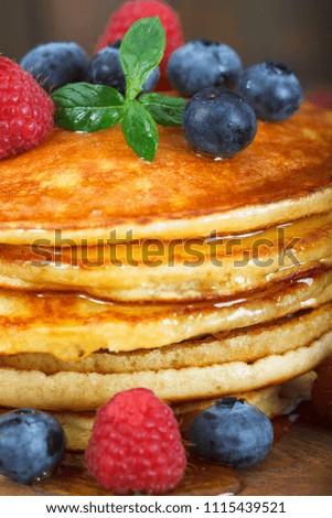 Stack of freshly baked american pancakes with maple syrup, blueberries and raspberries on top. Closeup image.
