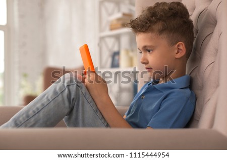 Adorable boy. Sweet adorable curly handsome boy feeling rested while watching funny cartoon on laptop sitting in armchair