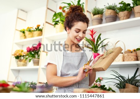 Beautiful gift. Pleasant nice woman standing in the flower shop while finishing wrapping the gift