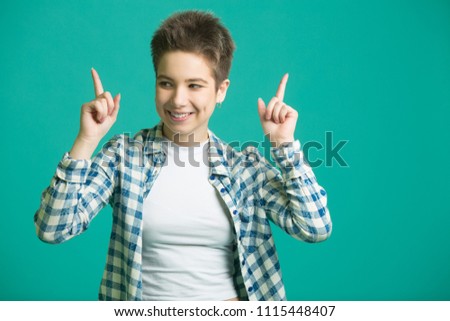 beautiful young girl with short hair in a shirt on a blue background pointing with her finger