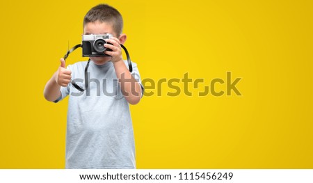 Dark haired little child holding vintage camera happy with big smile doing ok sign, thumb up with fingers, excellent sign