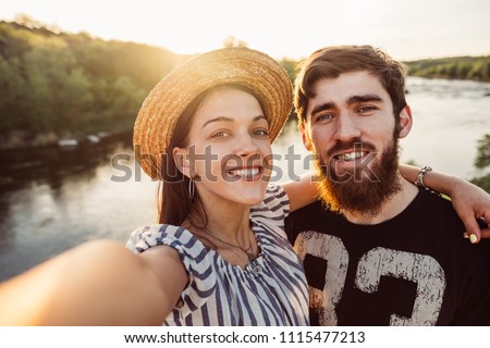 Happy young couple talking on video chat mobile phone app, taking selfie for social media. Woman and man traveling outdoor on romantic vacation, making nature landscape photo, chatting with friends.