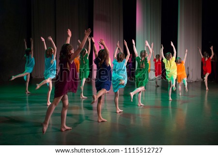 Girls in colorful dresses dance on stage barefoot. Royalty-Free Stock Photo #1115512727