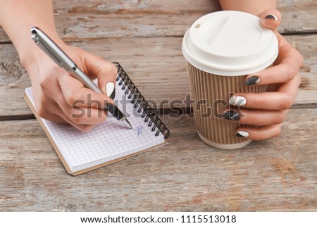 Manicured hand writing on notebook. Female manicured hands with pen, paper notebook and cardboard cup of coffee.