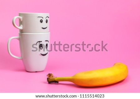White ceramic mugs with painted funny faces and fresh fruit, healthy food, benefits and vitamins. Banana.