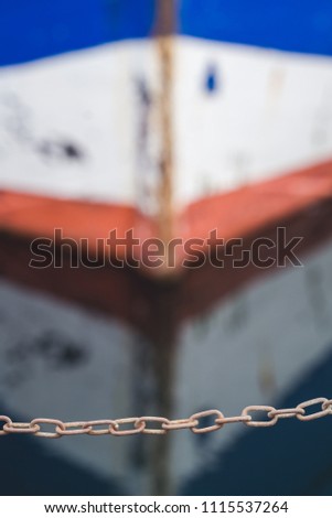 Small protective chain on the edge of a landing in a marina with a water reflection of a small empty fisherman boat in the background