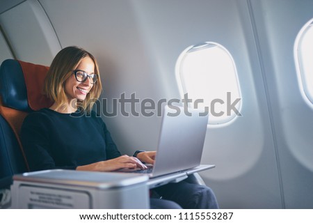 Traveling and technology. Flying at first class. Pretty young businees woman working on laptop computer while sitting in airplane. Royalty-Free Stock Photo #1115553287