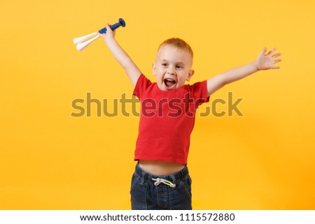 Little cute kid baby boy 3-4 years old, football fan in red t-shirt holding in hand pipe, blowing isolated on yellow background. Kids sport family leisure lifestyle concept. Copy space advertisement