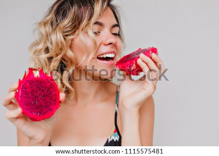 Close-up portrait of attractive tanned woman with short hairstyle eating dragon fruit. Studio shot of refined girl enjoying juicy red pitaya.