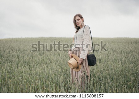 Girl in eco style clothes posing in nature background. Portrait of young woman in boho hat. Pretty ethno stranger in field.