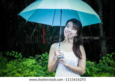 Portrait picture of beautiful Asian woman in a park with blue umbrella while raining