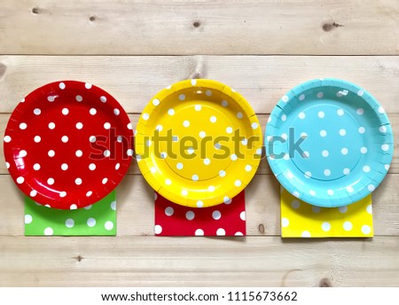 Colorful polka dot paper plate and napkin on wooden board background.
