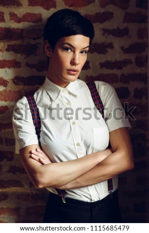 Beautiful young woman, model of fashion, with very short haircut, looking at camera with a brick wall in the background. Beauty and hairstyles concept.