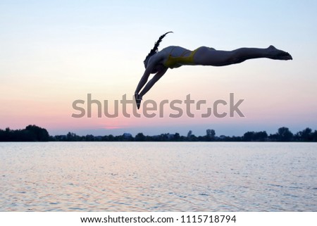 Silhouette of a girl jumping into the water in the evening
