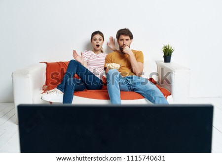 an indignant woman and a man with popcorn watching TV                               