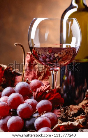 Red wine on a table with grapes and dried up vine leaves .