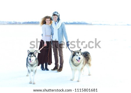 Woman and man walking with huskies in white winter background. Concept of strolling with dogs in Alaska.