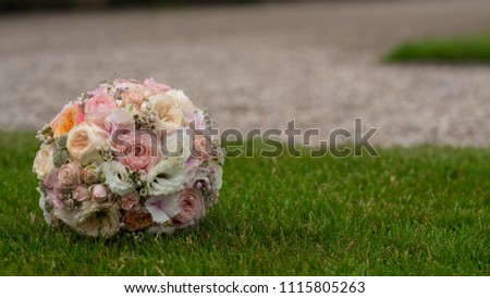 Closeup view of one big round beautiful fresh wedding bouquet of rose flowers pink white and yellow pastel colors lying on green grass sunny day outdoor, horizontal picture