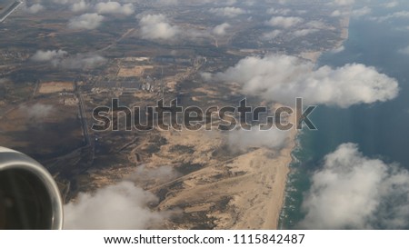 White  fluffy clouds over the buildings and the Mediterranean Sea of ​​Tel-Aviv, Israel.  A picture from the window of a passenger airplane from above