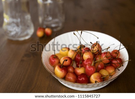 Red and yellow cherry in white plate at wooden background